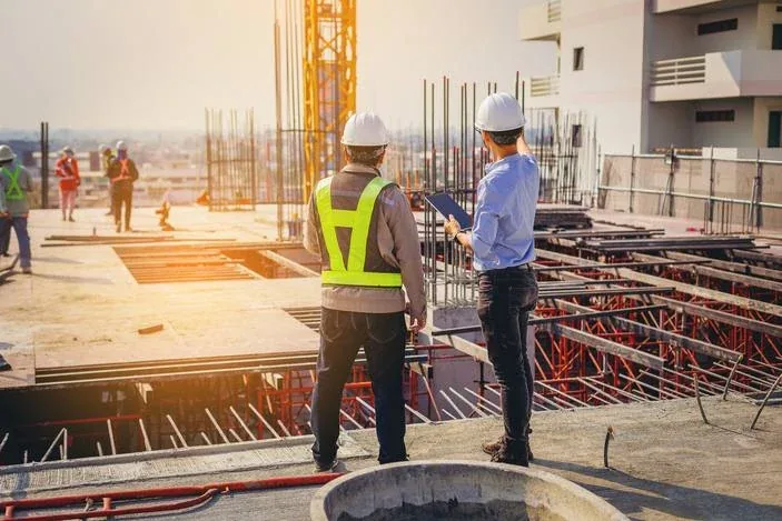 Zwei Bauleiter mit Schutzhelmen und Tablet auf einer Rohbau-Baustelle