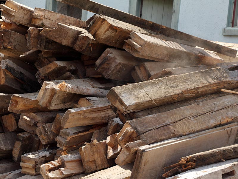 Mehrere alte Holzbalken liegen gestapelt vor einem Haus.