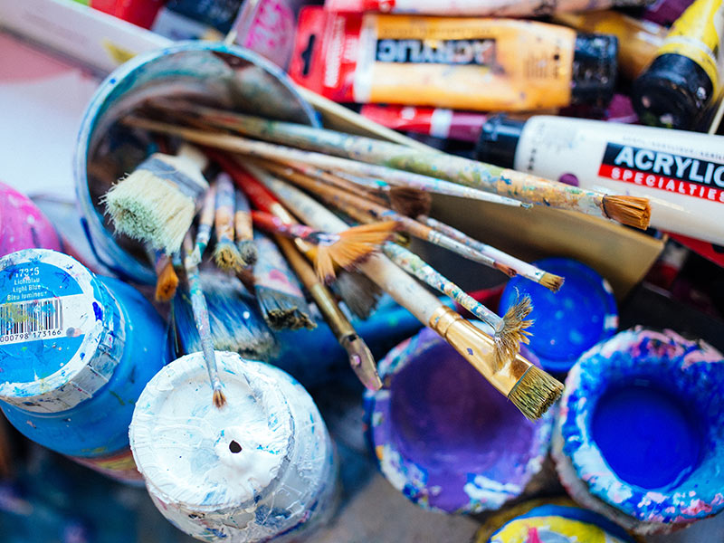 Acrylfarben, Pinsel und Farbschalen liegen auf einem Tisch.