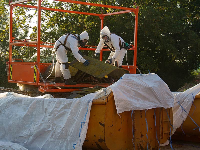 Zwei Personen in Schutzkleidung entsorgen Asbest in einem Asbestcontainer.