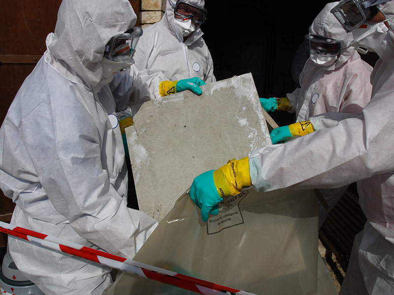 Personen in Schutzkleidung packen eine Asbest-Leichtbauplatte in einen Big Bag.