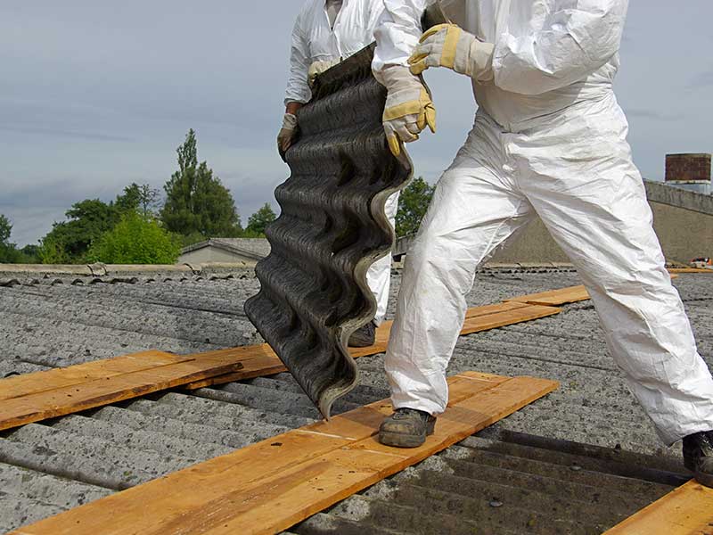 Zwei Personen mit Schutzkleidung demontieren Wellasbest auf dem Dach.