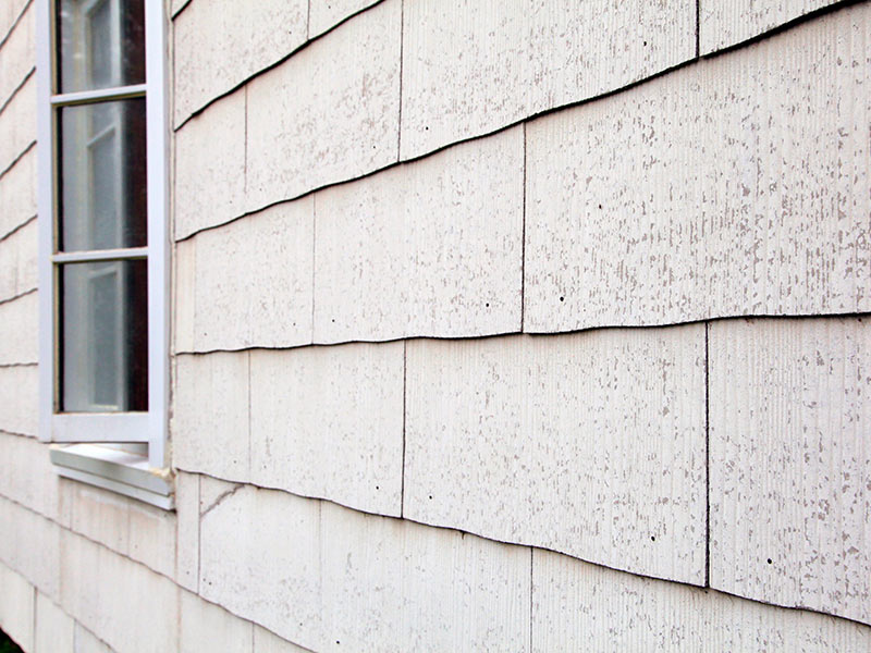 Hellgraue Asbestplatten an einer Fassade mit Fenster.