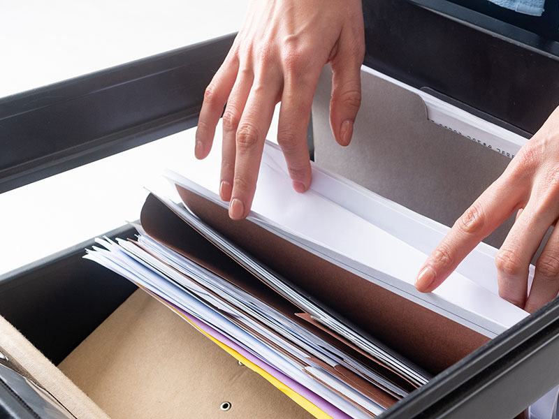 Person durchsucht Aktenschrank mit Papierakten.