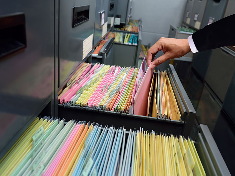 Person durchsucht archivierte Akten in einem Aktenschrank.