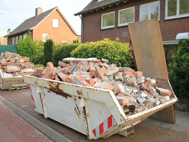 Ein mit Bauschutt gefüllter Container steht vor einem Haus.