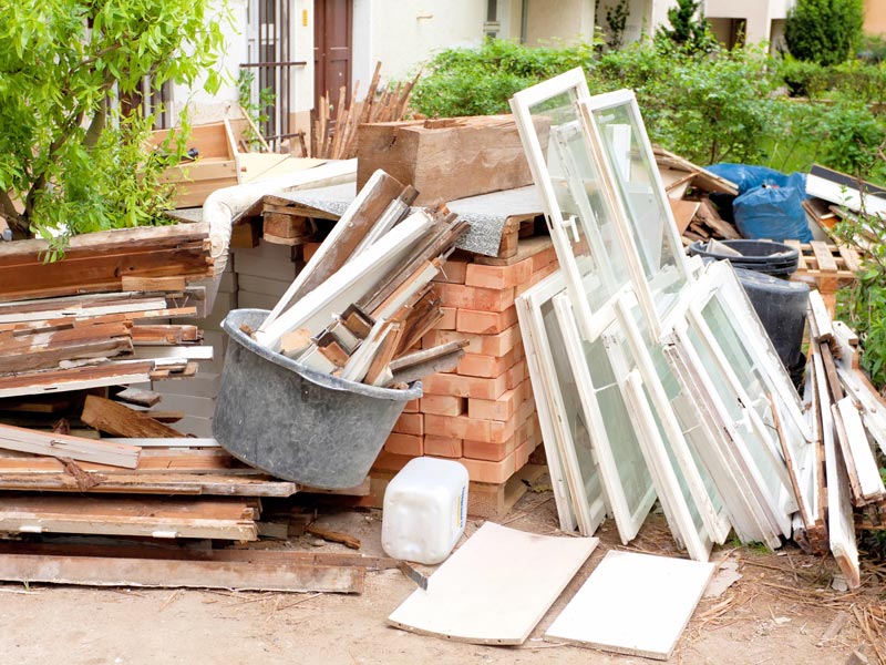 Baustellenmischabfall wie Fenster, Ziegel und Holz vor einem Haus.