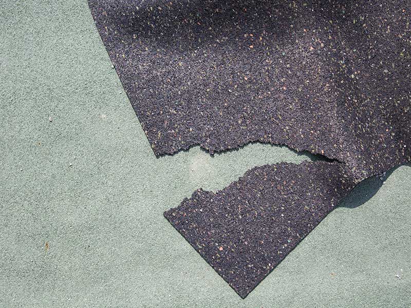 Zerrissene Dachpappe aus Bitumen liegt auf einem glatten Boden.