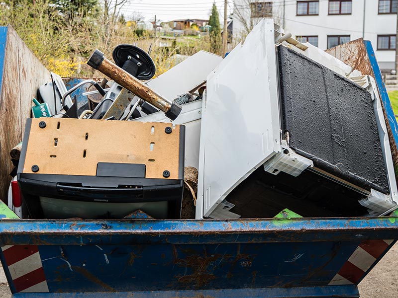 Mehrere große Elektrogeräte liegen in einem gefüllten Abfallcontainer für Elektroschrott.
