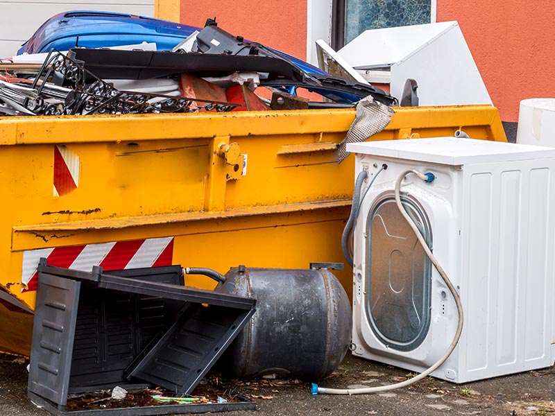 Ein mit Elektrogeräten befüllter Container steht vor einem Haus.