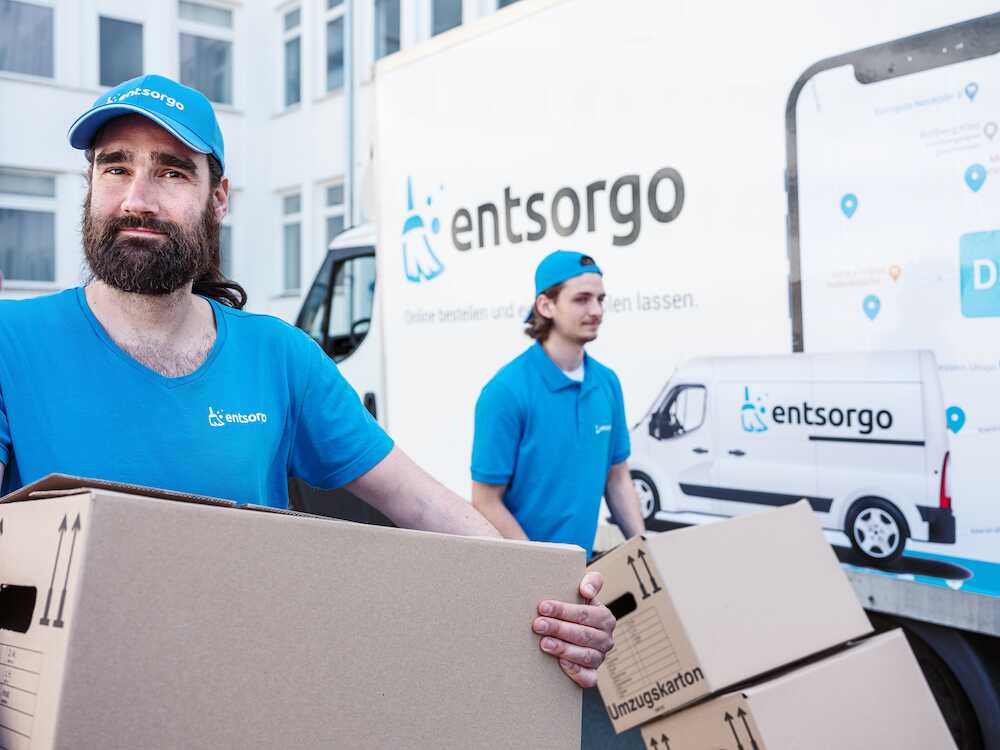 Das Bild zeigt: unserere Entrümpler bei einer Entrümpelung in einem Büro in Berlin. Die beiden Mitarbeiter stehen vor einem entsorgo Transporter