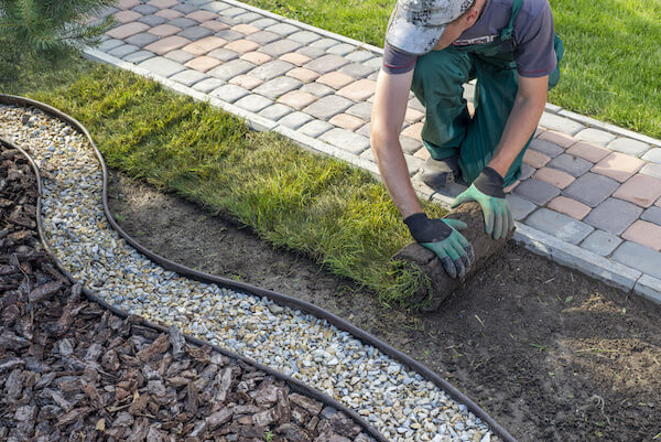 Dieses Bild zeigt einen Arbeiter bei der Verlegung von Rollrasen und dient der Verdeutlichung des Themas 'Entsorgungsservice für den Garten und Landschaftsbau in Berlin'.