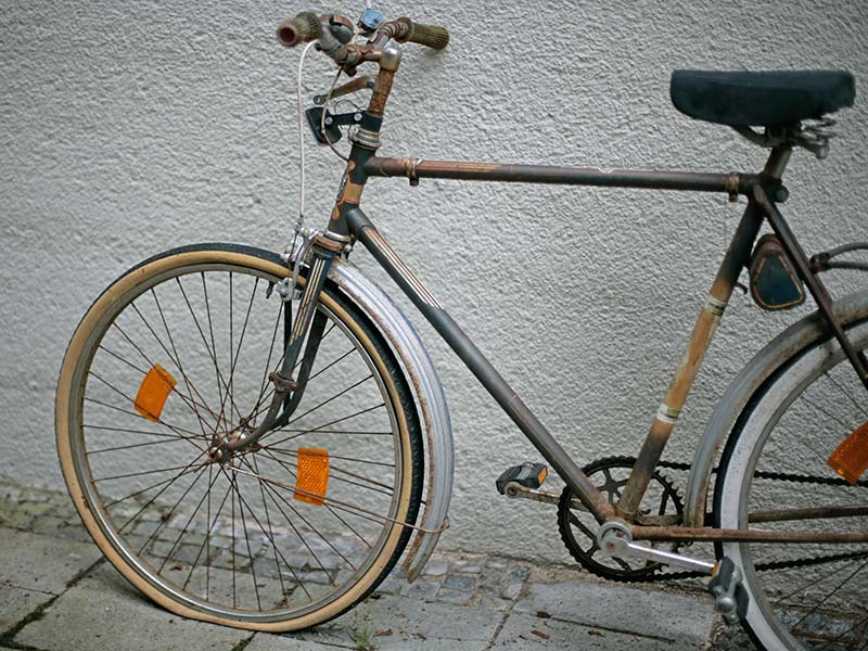 Altes Fahrrad mit platten Reifen lehnt an einer Hauswand.