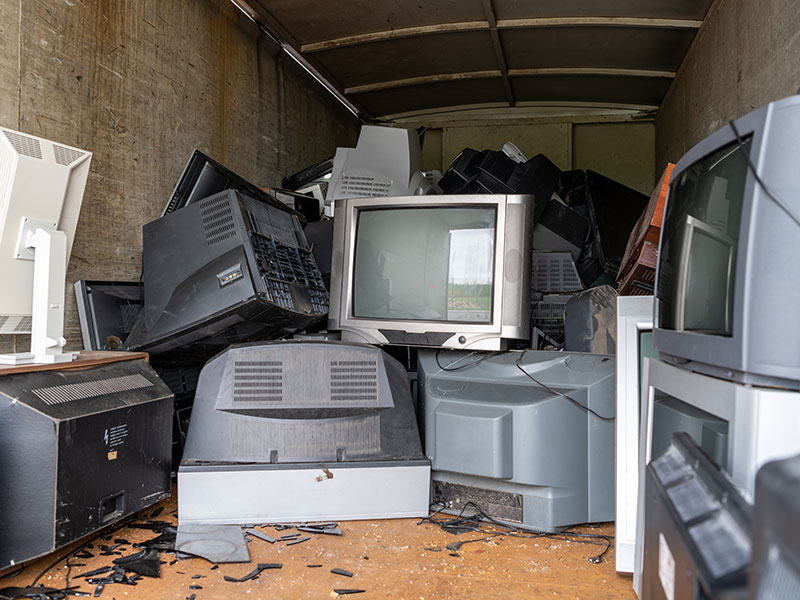 Mehrere Fernseher liegen zum Entsorgen in einem Container.