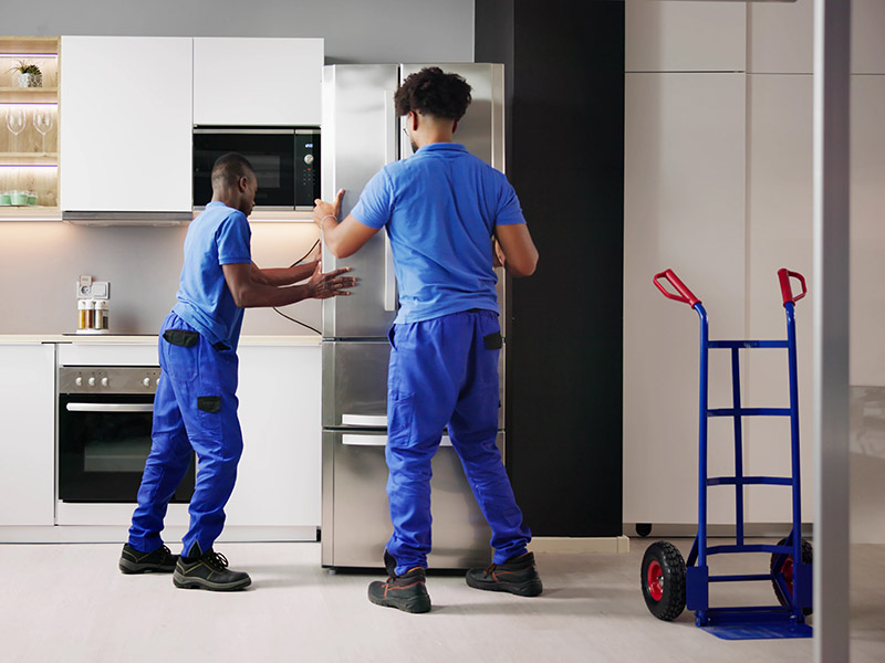 Zwei Elektriker platzieren einen neuen Kühlschrank mit Tiefkühler in einer Küche.