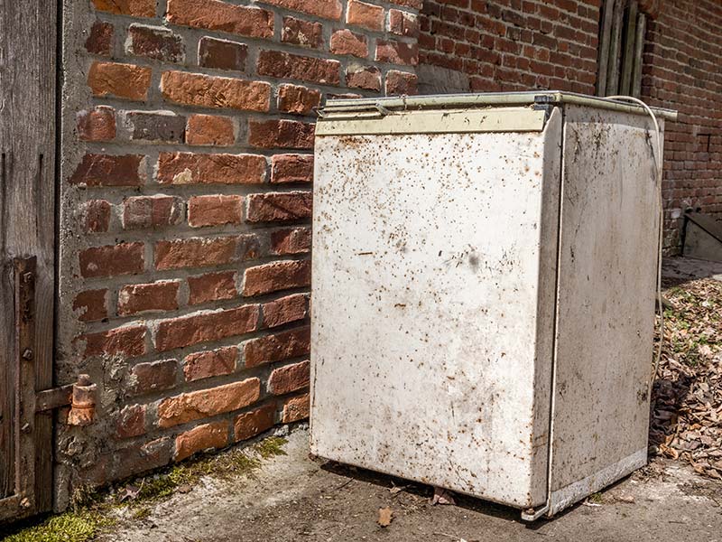 Schmutziger zu entsorgender Gefrierschrank steht vor einer Hauswand.