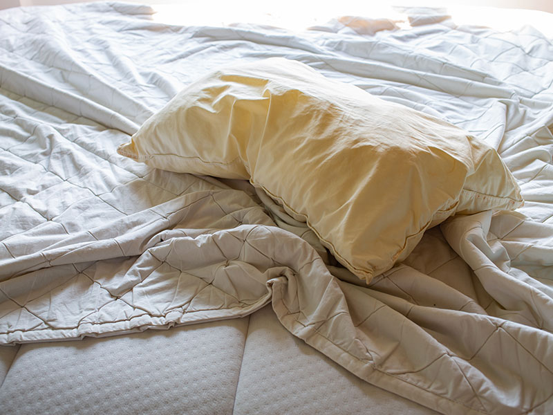 Altes Kopfkissen und Bettdecke liegen zerknüllt auf einer Matratze.