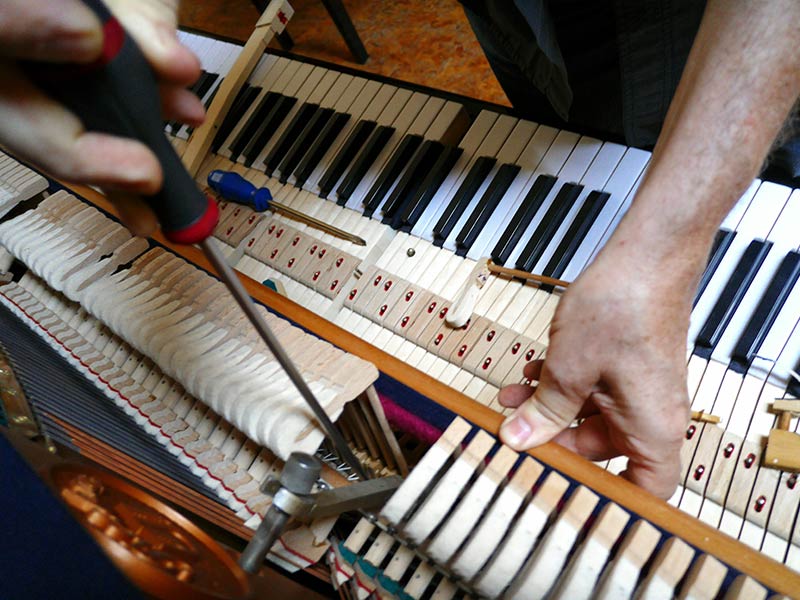 Person arbeitet mit einem Schraubendreher an einem geöffneten Klavier.