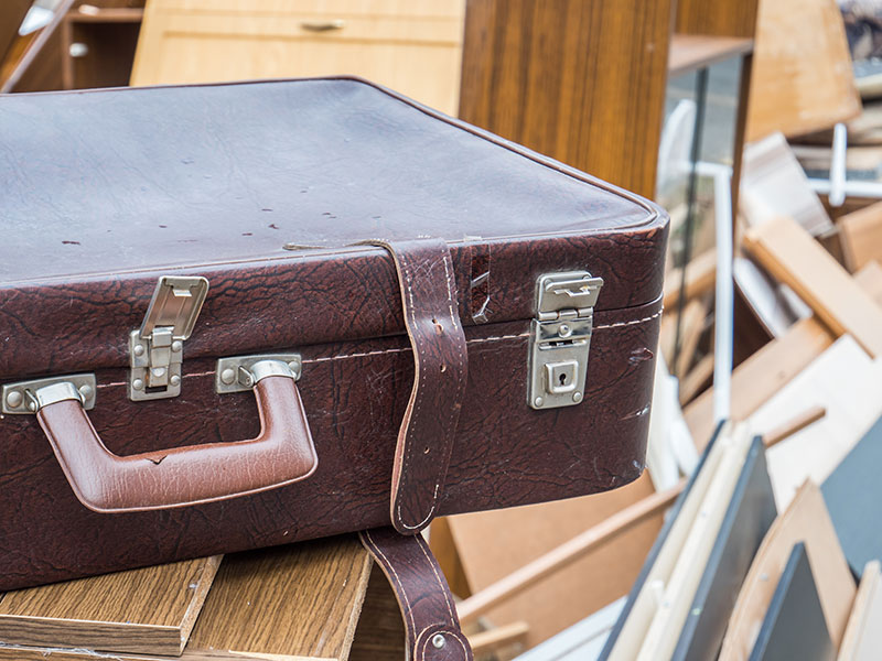 Alter Koffer aus Leder liegt neben weiterem Sperrmüll auf einem Haufen.