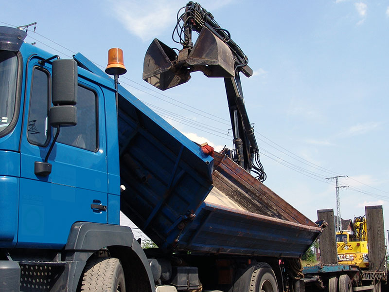 LKW mit einem leeren, gekippten Container auf der Ablagefläche und einem Kranarm.