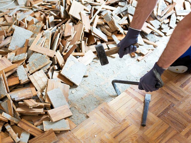 Person mit Hammer und Brechstange in der Hand entfernt Parkettboden.