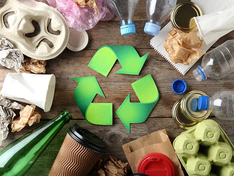 Verschiedene Abfallsorten liegen um ein Recycling-Symbol herum.