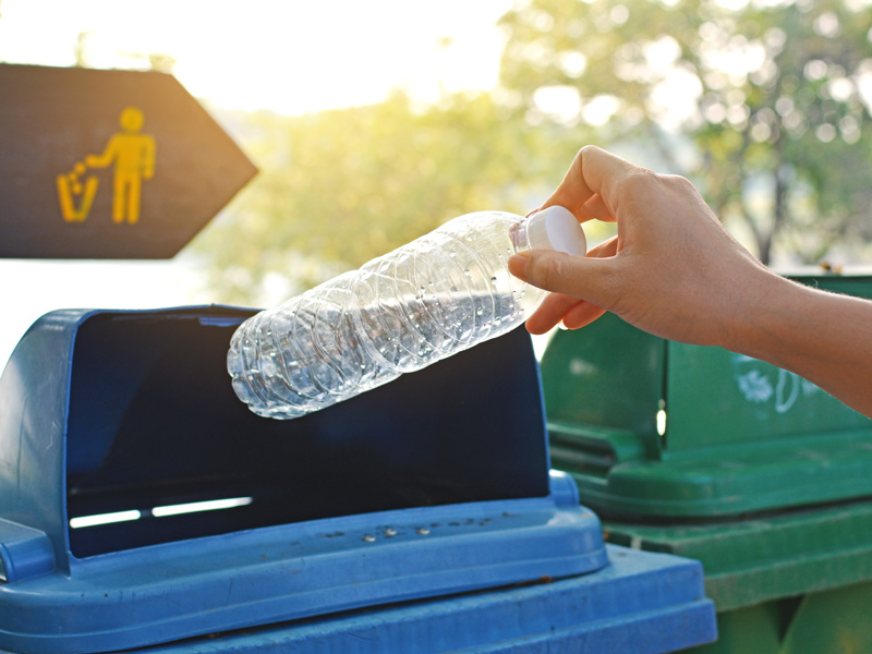 Person wirft Plastikflasche in einen Mülleimer.