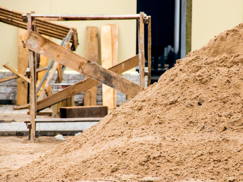 Ein Sandhaufen vor einer Baustelle mit Holzbrettern positioniert.