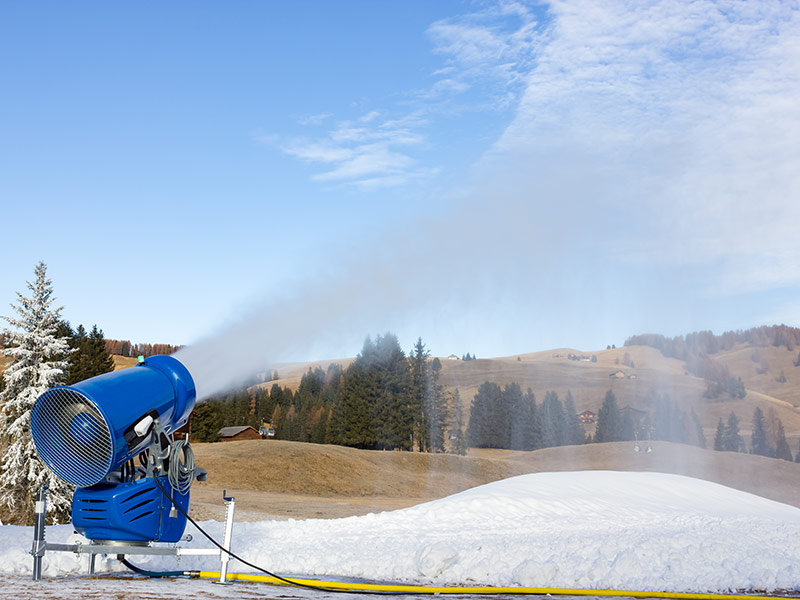 Schneekanone schießt Kunstschnee auf eine ansonsten schneefreie Fläche.