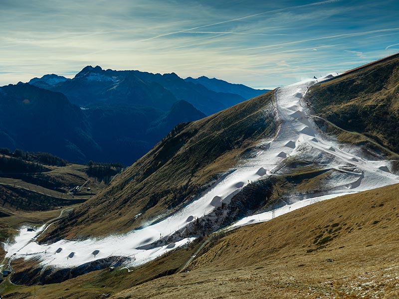 Aufnahme eines Berges, wo lediglich die Piste mit Schnee bedeckt ist.