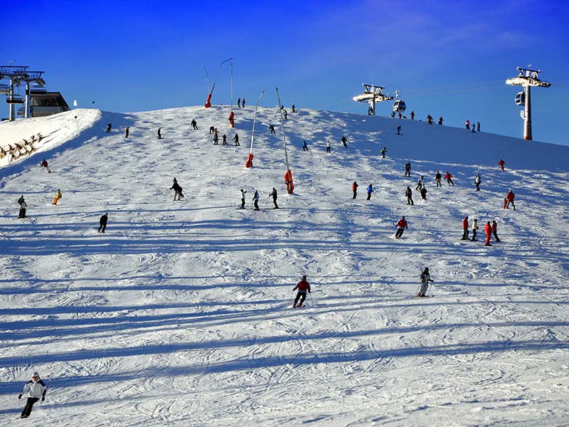 Skipiste mit einigen Skifahrern und Snowboardern bei der Abfahrt.