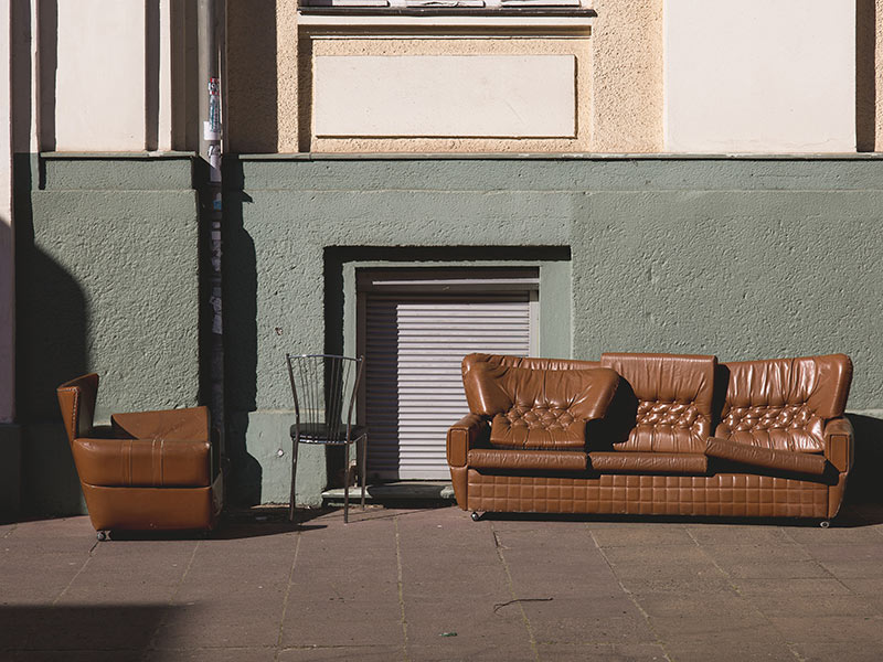 Ein Sessel und ein Sofa in brauner Lederoptik stehen auf der Straße vor einem Gebäude.