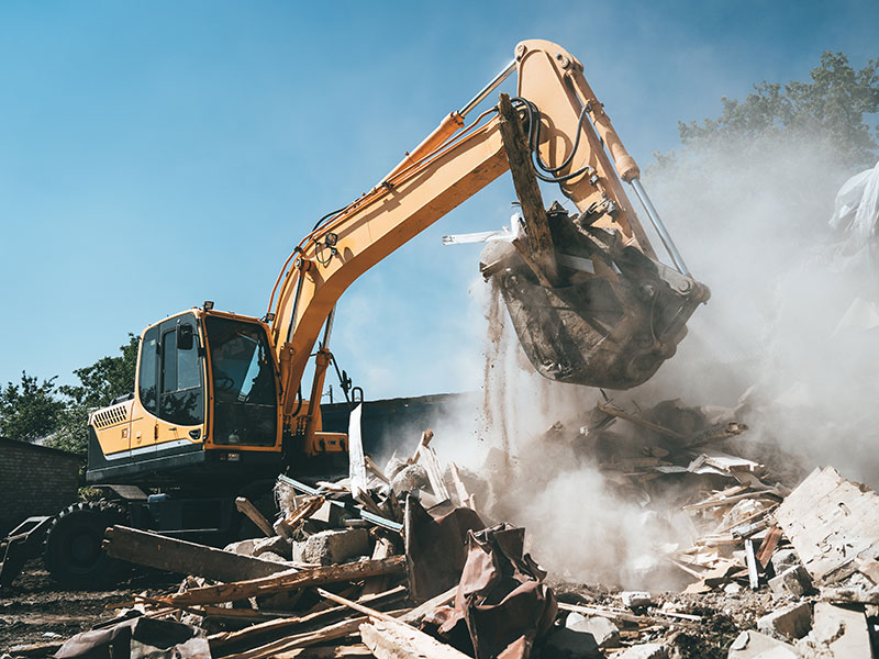 Bagger mit Schaufel voll Bau- und Abbruchabfälle auf einer Baustelle nach einem Abriss.