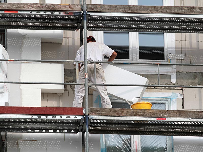 Handwerker klebt Styroporblöcke mit Putz an eine Hausfassade.