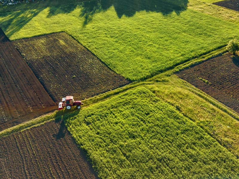 Vogelperspektive auf einen Traktor, der über Felder fährt.