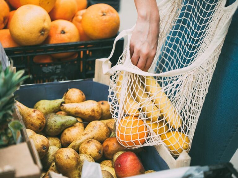 Person geht mit einem Stoffbeutel Obst einkaufen.