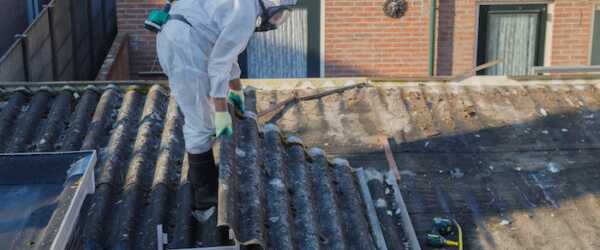 Personen mit Schutzanzug entfernen Wellplatten auf einem Asbestdach.